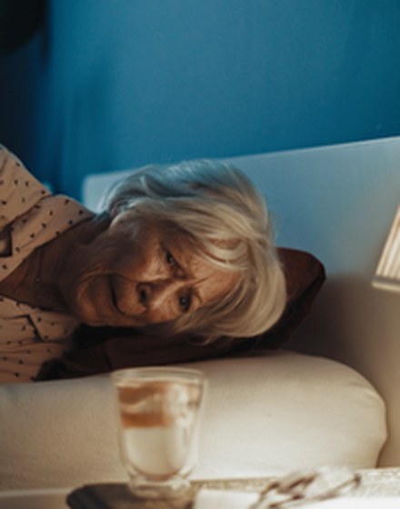 Beter Bed online campaign: an older woman lies awake in bed next to a bedside lamp